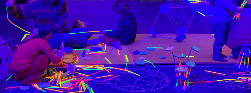 children playing with fluo-highlighted building blocks toys under a purple-black light